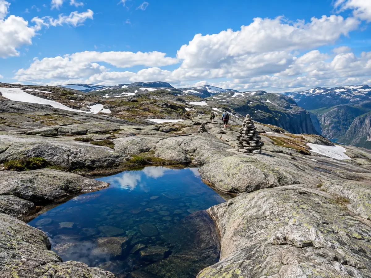 Le plateau de granit vallonné du Kjerag avec une mare et des randonneurs suivant des cairns