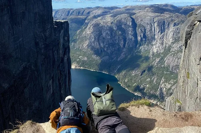 Zwei Wanderer liegen bäuchlings an einer Klippenkante und blicken in ein tiefes Fjordtal hinab