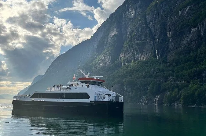 Eine weiße Passagierfähre auf stillem Wasser unter steilen, bewaldeten Fjordklippen